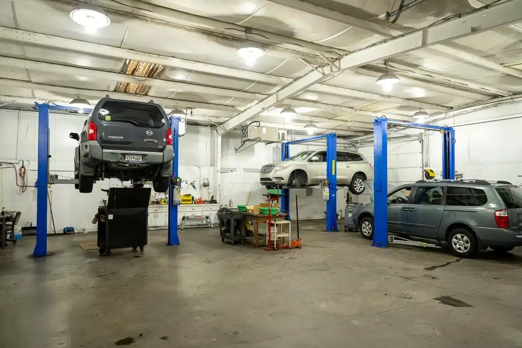 image showing fleet auto repair and maintenance services in Piedmont, SC. A brightly lit auto repair shop with three cars; two are elevated on blue hydraulic lifts for service, while one is parked on the ground. Tools and equipment are visible throughout the clean, spacious garage.