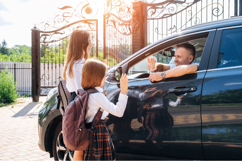 Car safety checklist. Auto repair in Piedmont, SC. Palmetto Complete Auto Care. Two schoolgirls with backpacks wave goodbye while their dad smiles from the driver’s seat of a black car, capturing a cheerful morning drop-off moment.