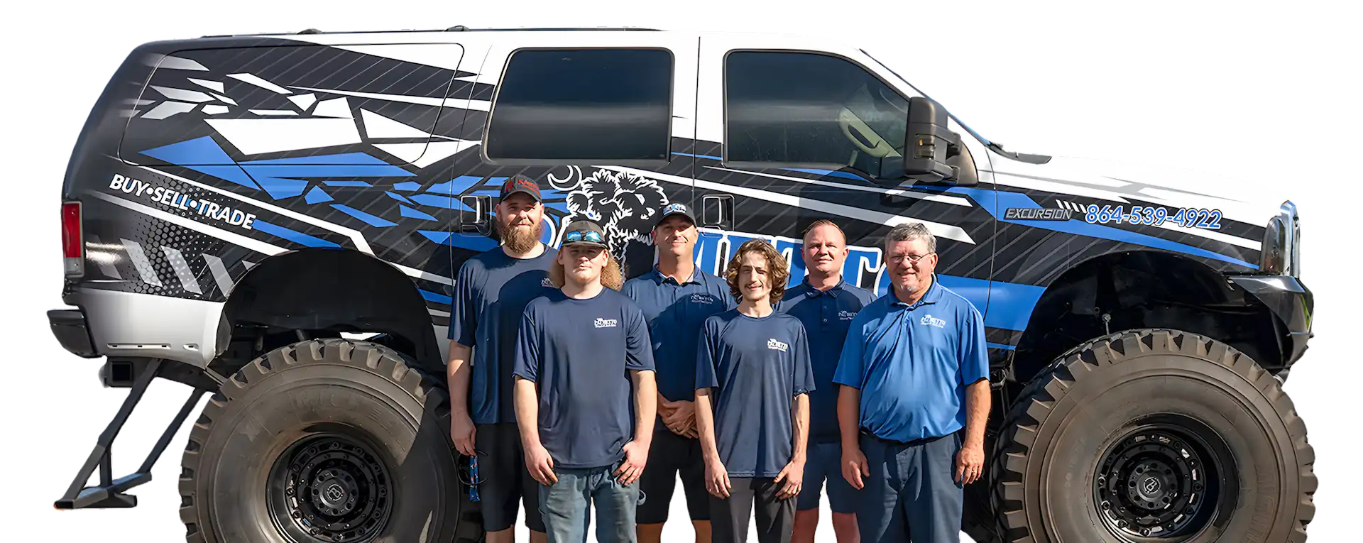 Six men in blue shirts stand in front of a large, lifted truck with oversized tires and a black, white, and blue graphic wrap displaying a phone number and text that says “BUY SELL TRADE.”.