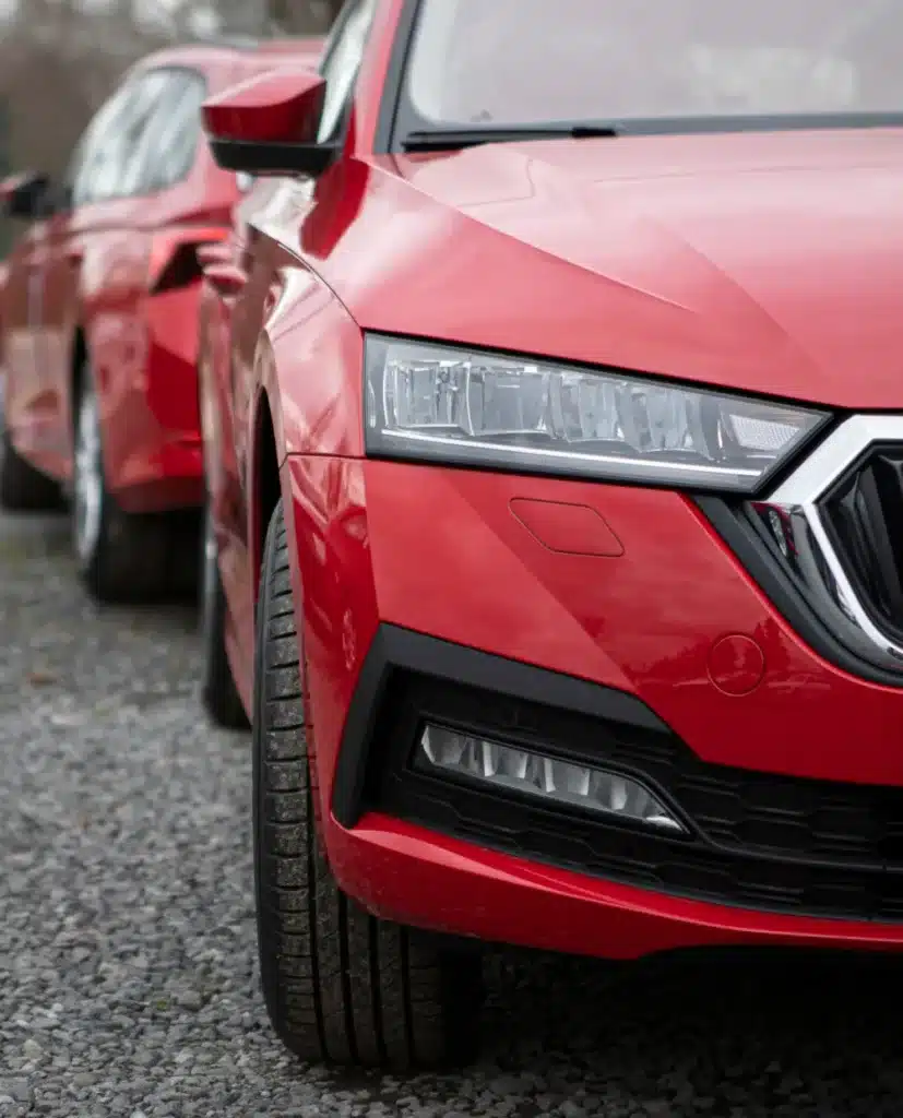 European auto repair by Palmetto Complete Auto Care shown with a close-up view of the front of a shiny red Mercedes Benz parked on a gravel surface, with another red car behind it, both partially visible.