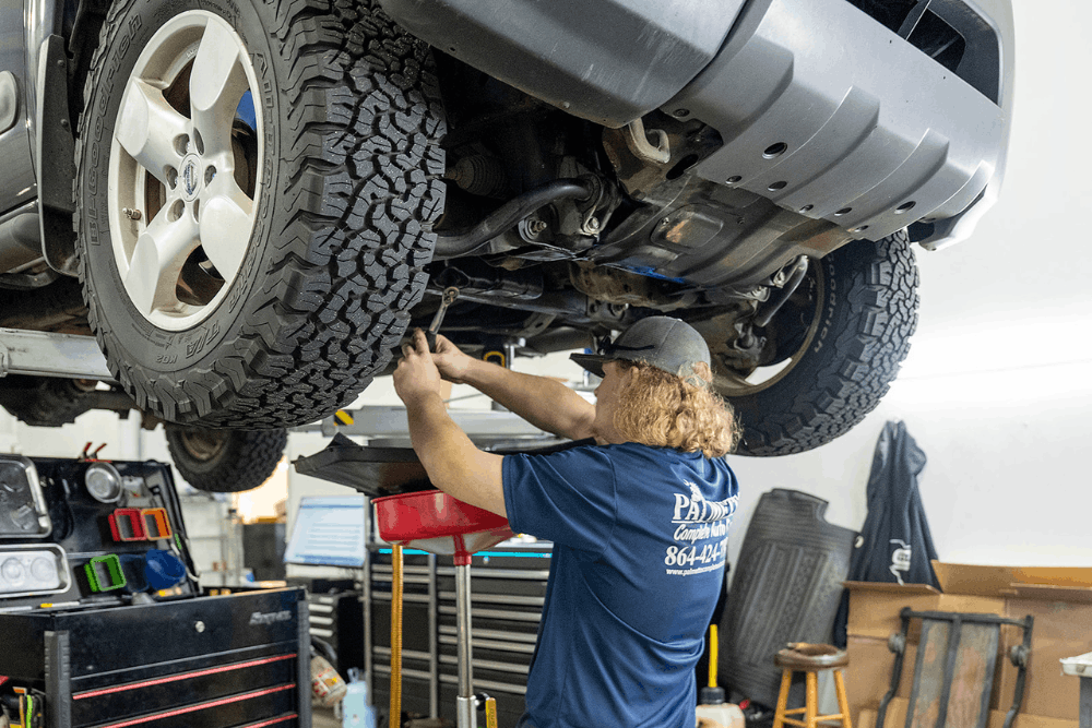Auto repair near Greenville, SC, at Palmetto Complete Auto Care. Image of a technician performing vehicle maintenance on a lifted SUV, highlighting expert diagnostics and repairs that help keep your vehicle safe, reliable, and ready for every drive.